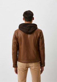 Bruine leren jas met een donkerbruine capuchon, met een getailleerd ontwerp en een gestructureerd oppervlak. Gecombineerd met beige broek, gezien van achteren.