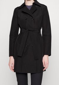 Trench-coat noir à double boutonnage, ceinturé à la taille, avec des épaules structurées. Comprend des boutons et une texture lisse.