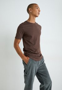 Brown cotton t-shirt with short sleeves, round neckline, and a relaxed fit, paired with gray striped cargo pants featuring side pockets.