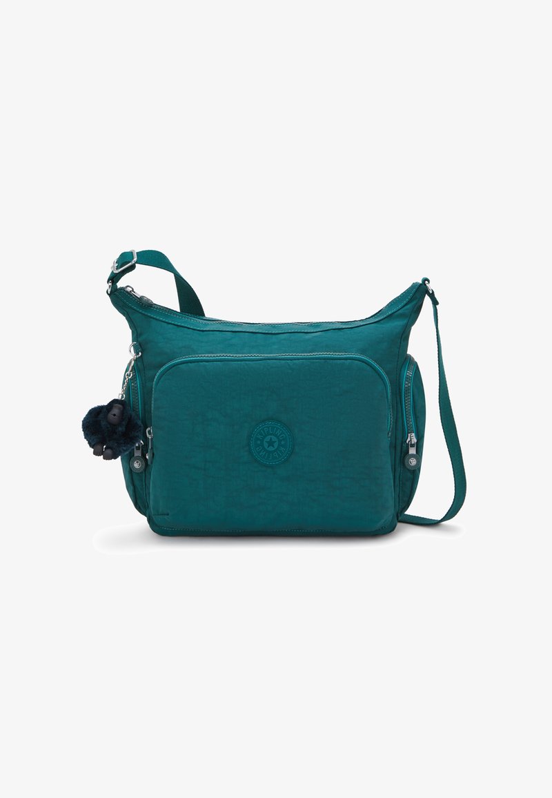 Teal crossbody bag with front zip pocket, adjustable strap, side zip pockets, and a small black plush monkey keychain attached.