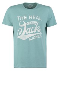 Tyrkysově zelené bavlněné tričko s krátkým rukávem, s velkým bílým potiskem textu: "THE REAL ORIGINALS Jack & Jones" na přední straně.