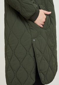 Quilted green jacket featuring a textured surface, side pocket, and snap buttons along the front. Soft material with a relaxed fit.