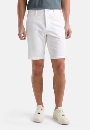 Weiße Baumwollshorts mit flachem Bund, Gürtelschlaufen und Taschen, kombiniert mit weißen Sneakers. Der Stoff hat eine glatte Textur.