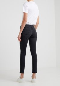 Jeans negros ajustados de cintura alta, con un sutil detalle en los bolsillos traseros, combinados con una camiseta blanca básica y zapatillas blancas.