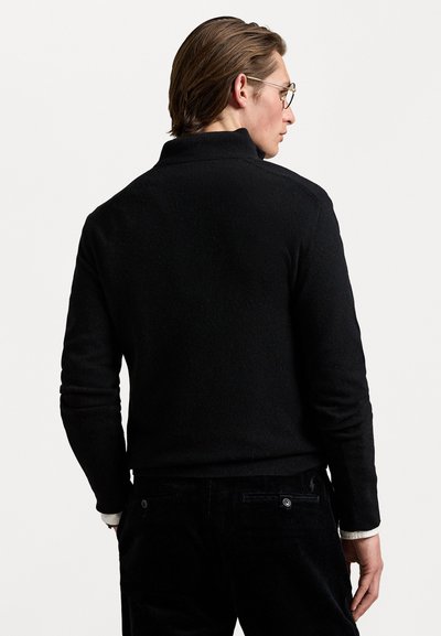 Pulover negru cu guler înalt, țesătură texturată, stil ajustat și manșete cu nervuri. Purtați-l cu pantaloni de catifea întunecată, evidențiind un design simplu.
