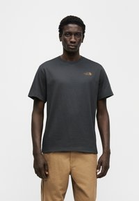 Μπλούζα κοντομάνικη από βαμβάκι σε σκούρο γκρι, με μικρό πορτοκαλί λογότυπο στο αριστερό στήθος, κλασικό στρογγυλό λαιμό και άνετη εφαρμογή.