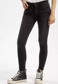 Czarne skórzane jeansy skinny z wysokim stanem, z subtelnią teksturą i detalami szwów, zestawione z czarno-białymi trampkami typu high-top.