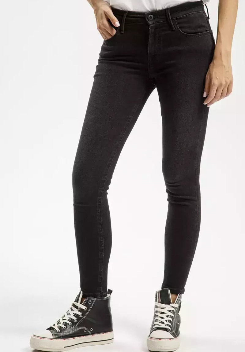 Czarne skórzane jeansy skinny z wysokim stanem, z subtelnią teksturą i detalami szwów, zestawione z czarno-białymi trampkami typu high-top.