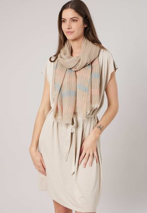 Femme portant une robe beige à manches courtes avec une taille nouée, accessoirisée d'une écharpe beige à rayures bleues et roses.