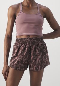 Top corto rosa fitted con spalline sottili abbinato a pantaloni corti marroni con un motivo astratto rosa e una vita elastica.