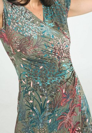 Primer plano de un vestido verde con un estampado colorido de hojas tropicales y detalles fruncidos en el lateral y el corpiño.