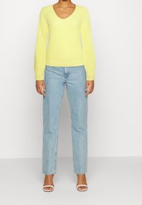 Gul stickad tröja med V-ringning, ribbade ärmslut och nederkant. I kombination med ljusblå raka jeans och vita klackar med remmar.