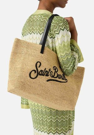 Persona che indossa un completo a zigzag verde e bianco che porta una grande borsa tote beige intrecciata con scritta nera "Saint Barth" e manici neri.