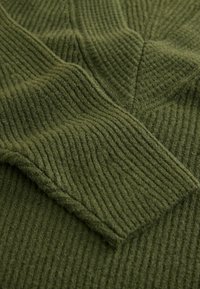 Groene ribstof met een getextureerd oppervlak, voorzien van een zachte, fleece-achtige afwerking en hoekige naaddetails.