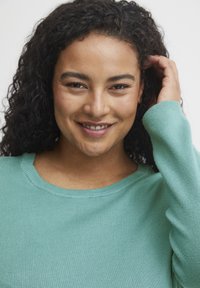 Maglione a maglia di un verde teal chiaro con colletto a girocollo e polsini a costine, che mostra una texture liscia e un design aderente.