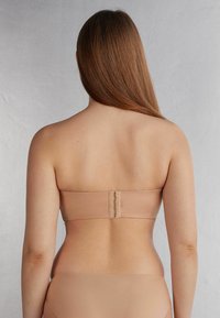 Naakt bandeau bh met een gladde textuur, voorzien van een haak- en oogsluiting aan de achterkant. Eenvoudig, naadloos ontwerp zonder bandjes.
