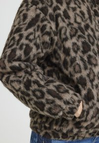 Veste en fausse fourrure imprimé léopard avec une surface douce et texturée et des manches longues, dotée d'une poche latérale visible à la taille.