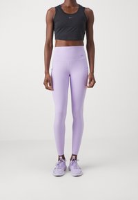 Zwarte, cropped sporttop gecombineerd met hoog-gesneden lavendelkleurige leggings. De leggings hebben zijzakken en zijn gemaakt van een gladde, elastische stof.