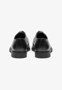 Zapatos de cuero negros con un acabado suave, diseño redondeado, suela de goma negra de perfil bajo, costuras visibles y un ligero detalle en el tacón.