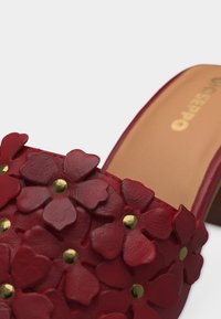 Κόκκινο δερμάτινο σανδάλι με τετράγωνο τακούνι, διακοσμημένο με στρωματοποιημένα σχήματα λουλουδιών και μικρές στρογγυλές χρυσές καρφίτσες στον πάνω λουράκι.