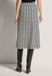 Hahnentrittmuster Midi-Rock in Schwarz und Weiß mit einem ausgestellten Saum, kombiniert mit knielangen schwarzen Stiefeln. Glatte Textur.