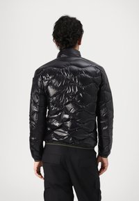 Giacca a vento nera in materiale lucido e trapuntato. Caratterizzata da un colletto alto, polsini elasticizzati e un design aderente.