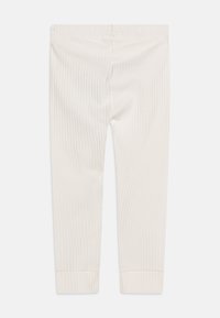 Leggings a coste in un beige chiaro, con un design aderente e una texture morbida, con polsini alla caviglia. Nessuna ferramenta o motivo visibile.
