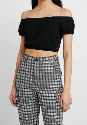 Sort off-the-shoulder cropped top med korte puffærmer, parret med høj talje sorte og hvide ternede bukser med lommer og knaplukning.