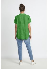 Green linen shirt with short sleeves, collar, and a slightly curved hem, paired with light blue jeans and white sneakers.