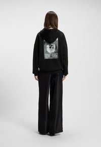 Felpa nera con cappuccio che presenta una stampa grafica sulla schiena, abbinata a pantaloni larghi neri lucidi. Tessuto morbido con vestibilità rilassata.