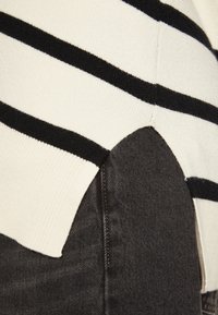 Sweter dzianinowy w czarno-białe paski; cechuje go zaokrąglona czarna dolna część. Miękka tekstura, standardowy krój i minimalnie widoczne szwy.
