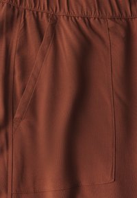 Roodkleurige stof met een gladde textuur heeft een zijzak en een elastische tailleband, wat een ontspannen ontwerp benadrukt.