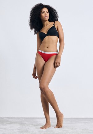 Zwarte gewatteerde beugelbeha met verstelbare bandjes en een rode slip met een witte Calvin Klein tailleband. Gladde stof en aansluitend ontwerp.