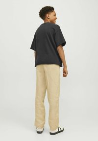 Svart bomulls T-shirt med kort ärm, i kombination med ljus beige linnebyxor. Outfiten kompletteras av vita skor med svarta accenter.