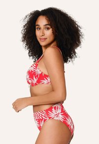Roter Bikini mit weißen tropischen Blattmustern, bestehend aus einem eng anliegenden Bralette und hochgeschnittenen Höschen. Glattes Material mit leichtem Glanz.