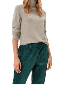 Pull à col roulé gris clair à manches longues, associé à un pantalon jogger en velours côtelé vert foncé avec poches zippées et taille à cordon de serrage.