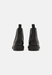 Botas Chelsea de cuero negro con una textura suave, paneles laterales elásticos y una suela de goma negra plana, que cuentan con tiradores traseros para ponerlas con facilidad.