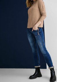 Maglia beige a maniche lunghe con texture abbinata a jeans skinny blu con finitura strappata, polsini arrotolati e stivali neri con tacco chunky.