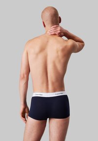 Boxeri din bumbac de culoare albastru marin, cu un brâu elastic alb încadrat cu brandingul "Calvin Klein", prezentați din spate pe un fundal neutru.