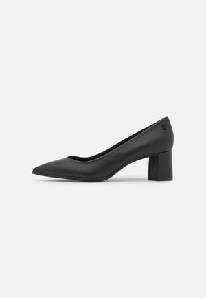 Zapato de tacón de cuero negro con punta afilada y un diseño elegante, equipado con un tacón cuadrado robusto. Presenta una textura suave y un detalle de marca sutil.