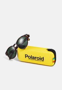Polaroid sunglasses with dark green lenses in a tortoiseshell frame, next to a yellow hard case featuring the Polaroid logo.