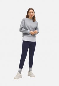 Sudadera gris con cuello redondo, superpuesta a una camiseta blanca, combinada con leggings azul marino y zapatillas blancas con calcetines a rayas grises y blancas.