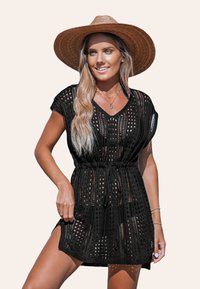 Abito nero lavorato a maglia con scollatura a V, maniche corte e vita con cordoncino. Presenta un motivo a trama aperta e spacchi laterali. Indossato con un cappello a tesa larga.