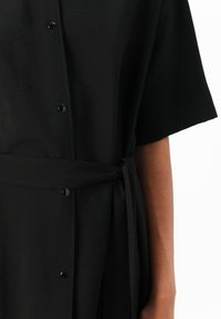 Black shirt dress featuring short sleeves, a button-up front, fabric belt at the waist, and smooth texture.