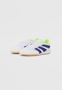 Zapatillas deportivas blancas con acentos morados, material de malla y sintético, área de los dedos perforada, forro interior verde y suela de goma.