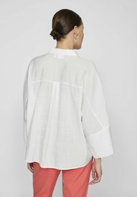 Camicia bianca oversize con colletto, spalle cadenti e dettagli plissettati sul retro. Tessuto morbido e leggero con una vestibilità rilassata.