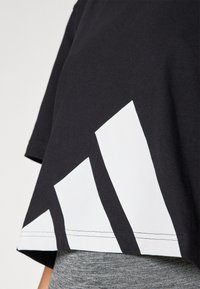 Fekete rövid ujjú, cropped póló, fehér geometrikus mintákkal az alján. Pamutból készült, sima tapintású.