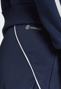 Marina idrottskläder i mjukt material, slim fit med vita accentfärger och "AEROREADY" märkning. Slät textur och modern design.