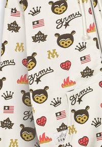 Sudadera con estampado sobre fondo blanco, que presenta caras de osos de dibujos animados, coronas, corazones, fuego y varios diseños de texto y emblemas en marrón oscuro, rojo y amarillo.