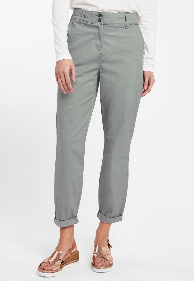 Pantalon gris clair, fuselé, avec une texture lisse, doté d'une fermeture à boutons et d'ourlets roulés. Assorti à des sandales métalliques à brides.